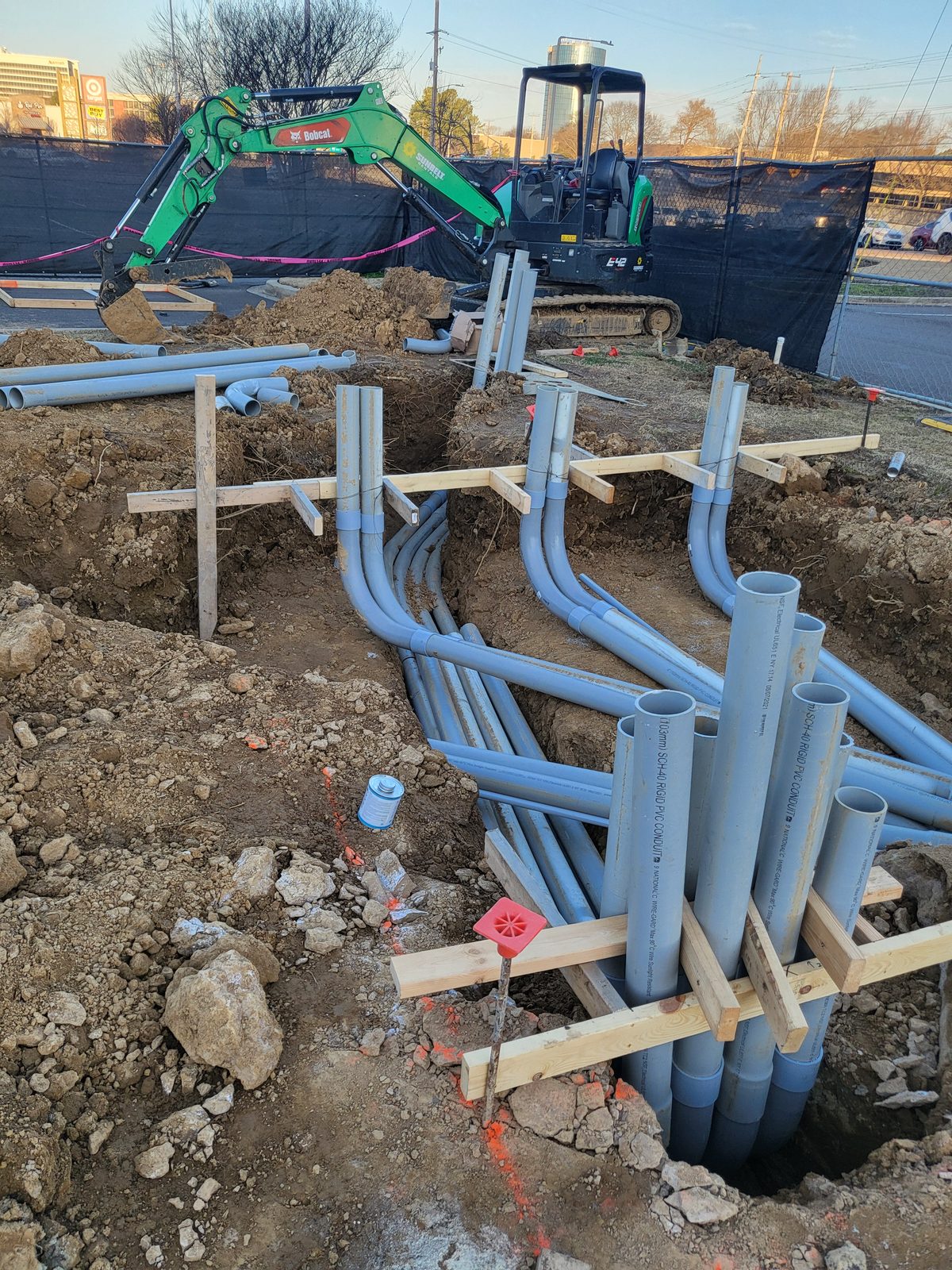 Excavator setting a large conduit duct bank